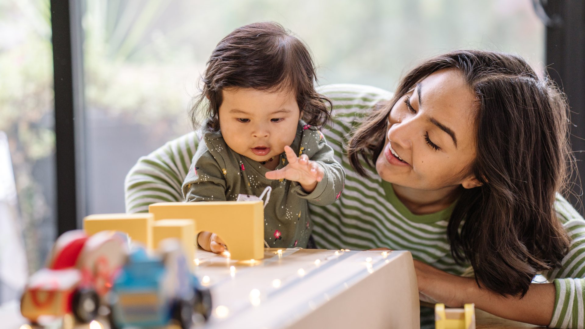 A young woman sharing toys with a toddler aged child at home