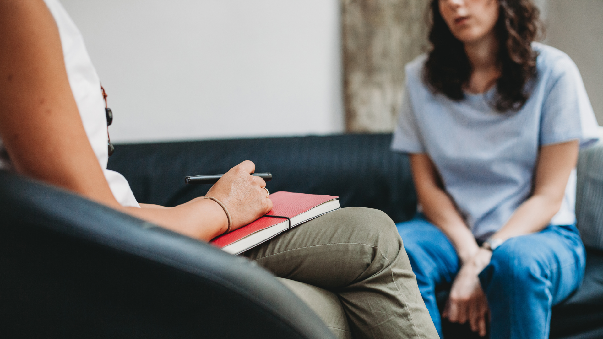 A young woman in a session with a support worker who is holding a red notebook and pen