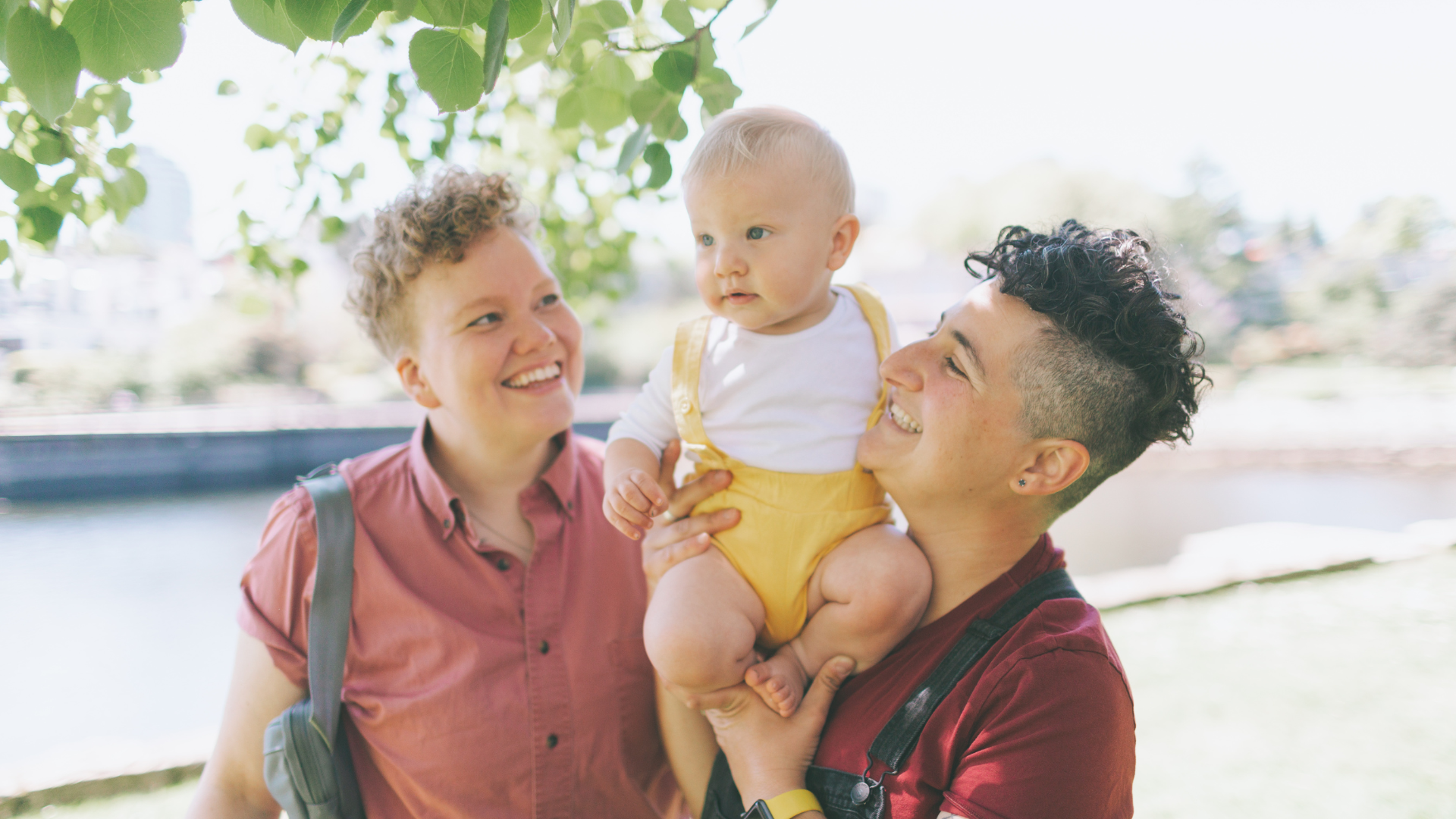 Lesbian couple carrying their baby and smiling